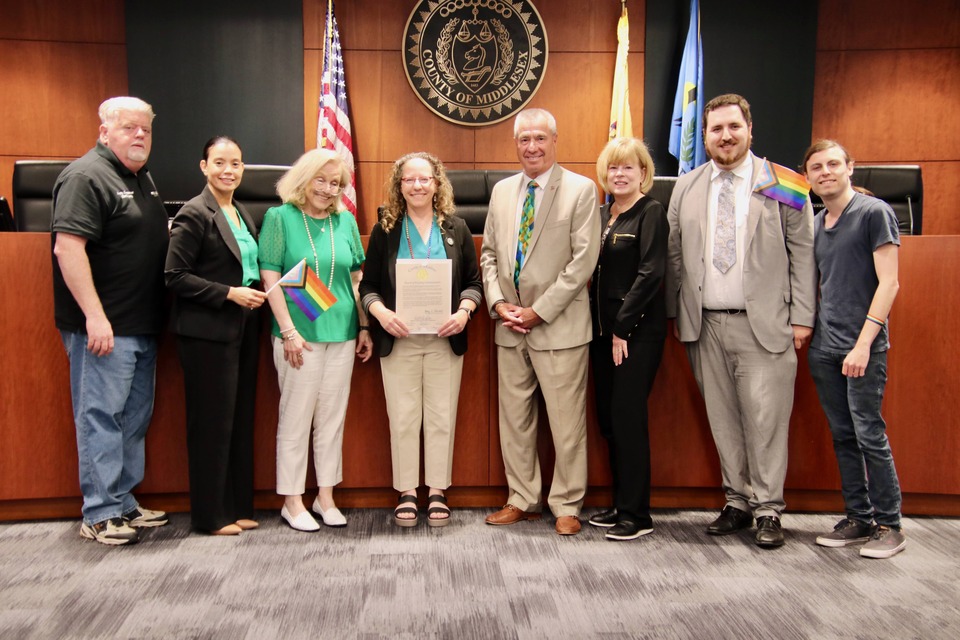 A group of people, some holding rainbow flags, stand around a woman holding an award.