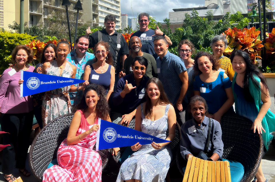 A group of people holding Brandeis flags pose together.